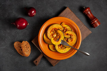 Delicious baked pumpkin on a brown plate, onion, bread and spices, top vew. The concept of healthy vegetable dishes. The concept of Thanksgiving