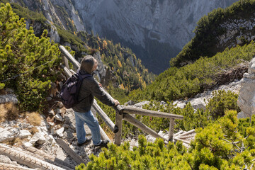 Gray-haired man standing on wooden steps on steep slope and looking at mountains covered with...