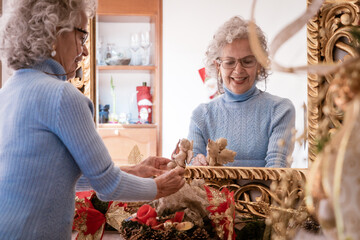 An elderly woman joyfully adorns her home for Christmas, standing in front of the mirror. This...