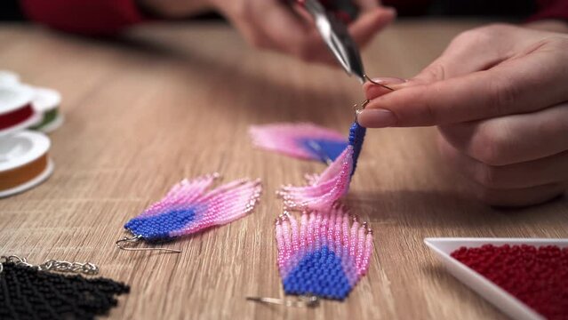 Creativity and hobby concept. Woman making triangular beaded earrings, close-up. Beads for needlework and beading.