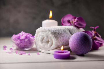 Obraz na płótnie Canvas purple bath bomb, sea salt crystals, towel and scented candles on wooden table. body skin care. wellness spa
