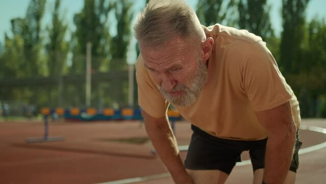 Caucasian exhausted elderly man runner tired jogging sport activity healthy lifestyle stadium outside running exercise fitness training outdoors old senior male have break rest hard breathing dyspnea