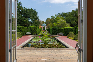 Naklejka premium a gorgeous summer landscape at New Orleans Botanical Garden with a pond covered in lily pads and colorful water lilies, lush green trees and grass, blue sky and clouds in New Orleans Louisiana USA