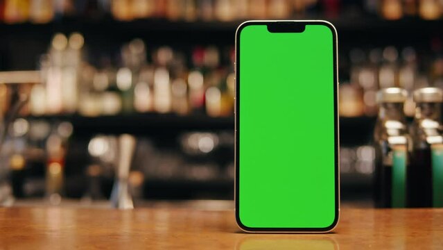 Smartphone with green screen on the table. Chroma key phone in the bar with some drink standing on bar counter. Delivery menu cafe bar restaurant