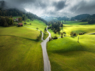 Aerial view of country road in green alpine meadows in overcast autumn day. Top view of rural road,...