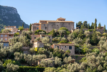 Fototapeta na wymiar Stunning cityscape of the small coastal village Deia in Mallorca, Spain. Traditional houses located in terraces on the hills surrounded by green trees. Spanish tourist destinations.