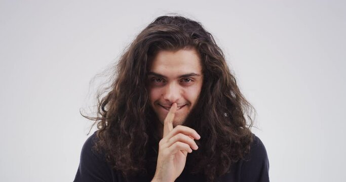Face, man and finger on lips in studio for secret, sign of privacy or scary mystery on white background. Portrait, creepy smile or quiet emoji for gossip, news of drama or whisper for sneaky surprise