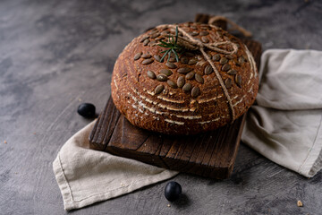 Baked sourdough bread from whole grain flour and pumpkin seeds on a grid, olive oil and black olive on a rustic wooden table. Artisan bread.