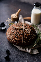 Baked sourdough bread from whole grain flour and pumpkin seeds on a grid, olive oil and black olive on a rustic wooden table. Artisan bread.