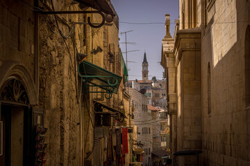 The tower of the Christian church is seen through the narrow street alley and historic buildings deep in Old Town of Jerusalem, Israel.