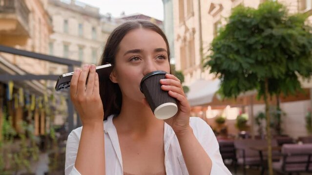 Caucasian young girl listening voice message phone smartphone connect outdoors European businesswoman drinking coffee on city street internet communication chat friends outside peaceful woman smile