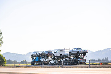 Blue classic old style big rig car hauler semi truck tractor transporting cars and crossovers on hydraulic semi trailer driving on the divided highway road in California