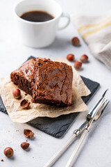 Pieces of chocolate brownies with hazelnuts and salted caramel on baking paper on a light background with a cup of coffee.