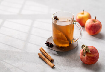 Homemade apple cider with apples and cinnamon in cup on a light background with fresh fruits, spices and shadows. The concept of an autumn or winter healthy drink.