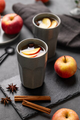 Obraz na płótnie Canvas Homemade apple punch or cider with apples and cinnamon in gray cups on a dark background with fresh fruits and spices close up.
