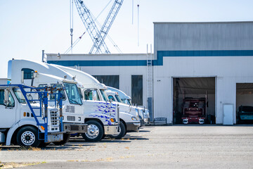 Different big rig semi trucks standing in row on industrial parking lot waiting for maintenance and...