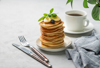 A stack of oat banana pancakes with fresh fruit slices, berries and honey on a light background...