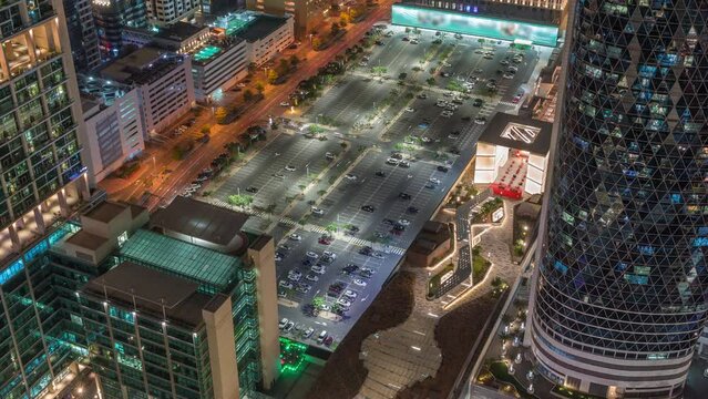 Skyline view of big parking lot surrounded by the high-rise buildings on Sheikh Zayed Road in Dubai aerial night timelapse, UAE. Illuminated skyscrapers in International Financial Centre from above