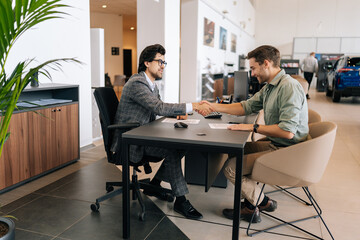 Wide shot of happy client male purchasing automobile in dealership, signing paper, shaking hands...