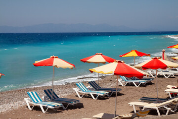 Beach on the Aegean Sea, Rhodes, Greece. Sun loungers and umbrellas on the sandy shore.