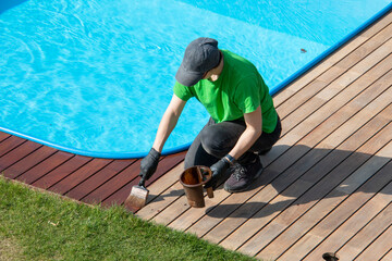Female worker painting exterior wooden pool deck with decking oil