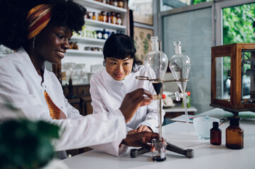 Multiracial pharmacists are using funnels and making traditional medicament in a vintage apothecary.