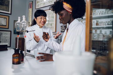 Cure discovery. Two multicultural pharmacists are cheering for a successful experiment in a vintage pharmacy.