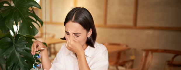 Working woman feeling tired, rubbing eyes after using laptop, having fatigue, sitting in cafe with...