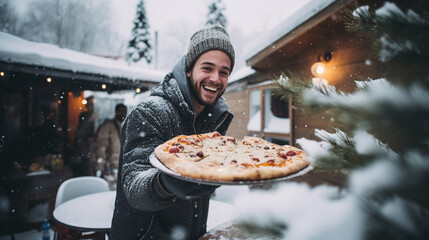 A happy young man with take-out pizza in his hands for a large group of friends in winter on the...