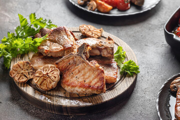 Grilled roasted bbq pork stakes served on wooden board on brown table background. Appetizing food