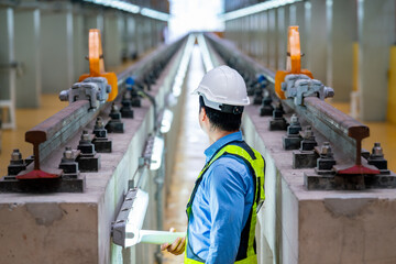 Back of professional engineer stand between railroad tracks of electrical or sky train and look to end of the rail in the factory workplace.