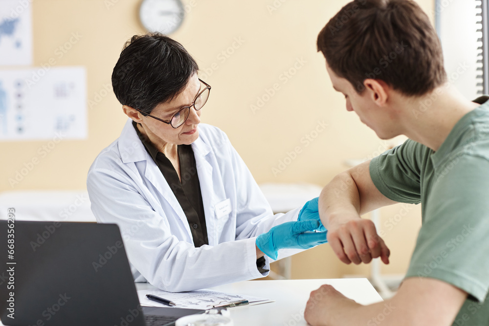 Wall mural Portrait of mature female doctor inspecting patient with skin rash during consultation in dermatology clinic