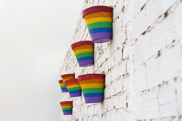 Flower pots painted in LGBT colors hang on a white brick wall.