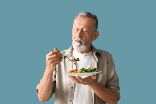 Mature man with tasty vegetables on blue background