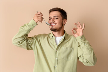 Young man with spoon showing OK on beige background