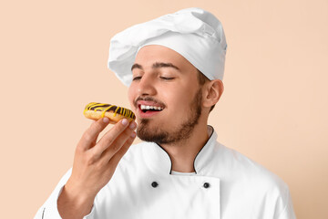 Male chef with tasty doughnut on beige background, closeup
