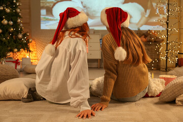 Young women in Santa hats watching Christmas movie on projector screen at home, back view