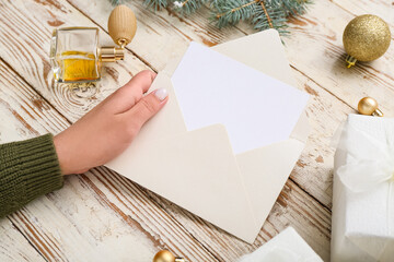 Woman with blank card, Christmas decor and gifts on white wooden background, closeup