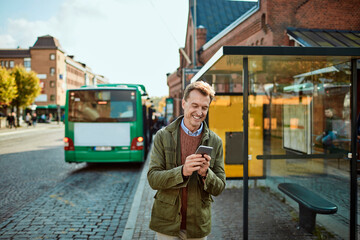 Man laughing while checking his phone at a bus station