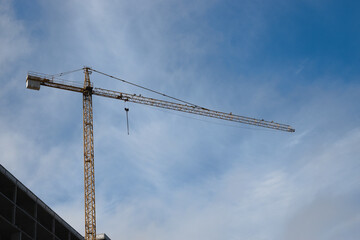 A tower crane at a construction site with a raised boom with blue sky in the background