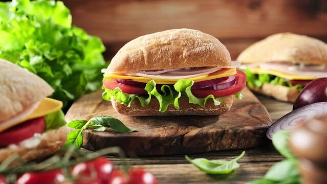 Sandwiches with fresh buns, ham, cheese, tomatoes, lettuce and mayonnaise sauce on the rustic wooden table. Stock footage 4k video.
