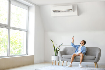 Young man switching on air conditioner at home