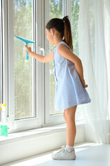 Fototapeta na wymiar Cute little girl cleaning window with squeegee at home