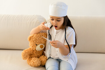 Little Doctor. Cute little girl with stethoscope and toy bear playing at home. Kid Girl Playing Vet...