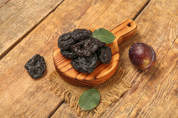 Board with tasty dried plums on wooden background