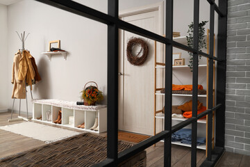 Interior of modern hallway with stylish clothes, shoes and autumn decorations, view through folding screen