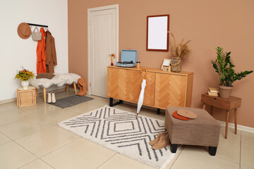 Interior of modern hallway with stylish autumn clothes, ottoman and wooden sideboard
