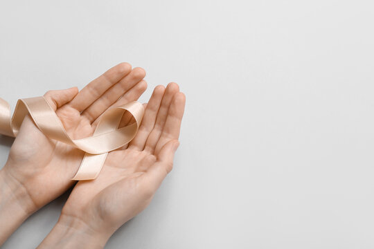 Woman with beige ribbon on light background. Uterine cancer awareness concept