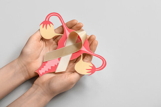 Woman with beige ribbon and paper uterus on light background. Cancer awareness concept