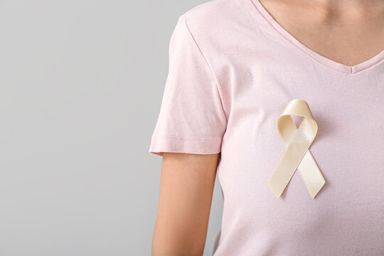 Woman with beige ribbon on light background, closeup. Uterine cancer awareness concept